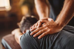 Two people in casual clothing stretching their joints in a sunny living room.