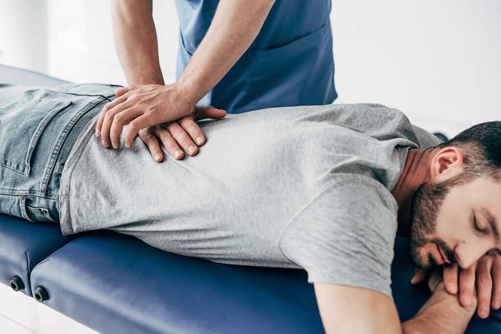 A chiropractor gently adjusting an adult patient's back on a padded treatment table.