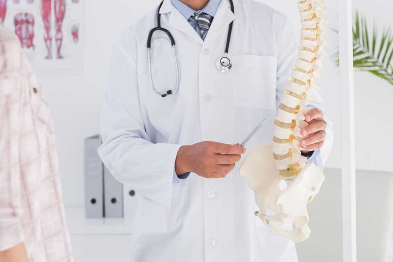 A chiropractor guides an adult through a gentle mobility exercise beside a treatment table.